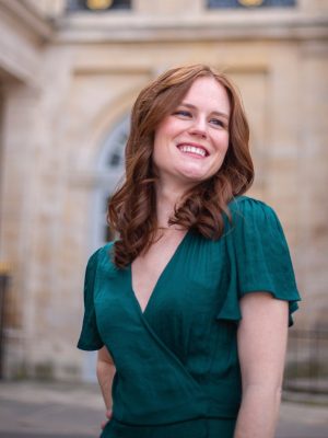 Brianna Murray, Soprano. In a green dress in front of a stone wall.